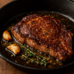Perfectly seared steak in a cast-iron pan with garlic and fresh thyme in melted butter