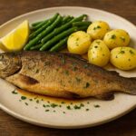 Grilled trout fillet with lemon slices, herbs, and vegetables on a rustic plate.